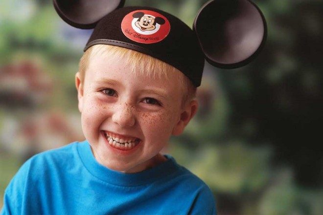 little boy wearing a Mickey Mouse hat smiling in a blue shirt
