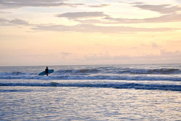 a beautiful horizon overlooking the waves at cocoa beach, a surfer with a surfboard in the distance